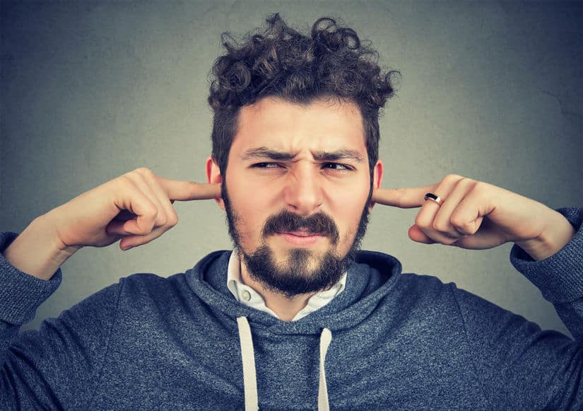 displeased man plugging ears annoyed by loud noise